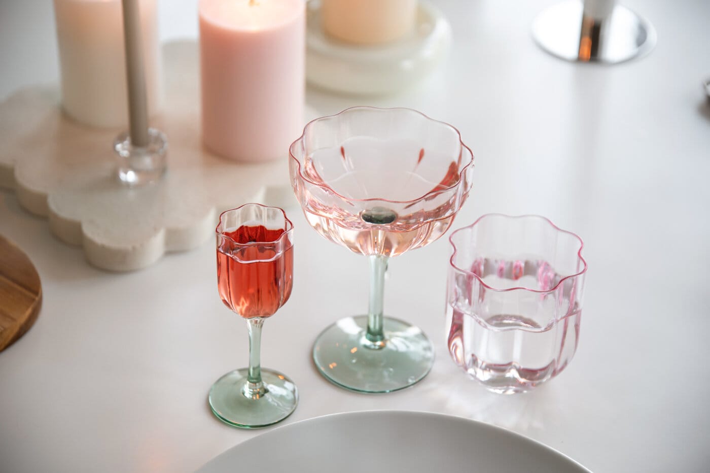 Glasserie i blomform uppställd på ett bord tillsammans med ljus och dukning.