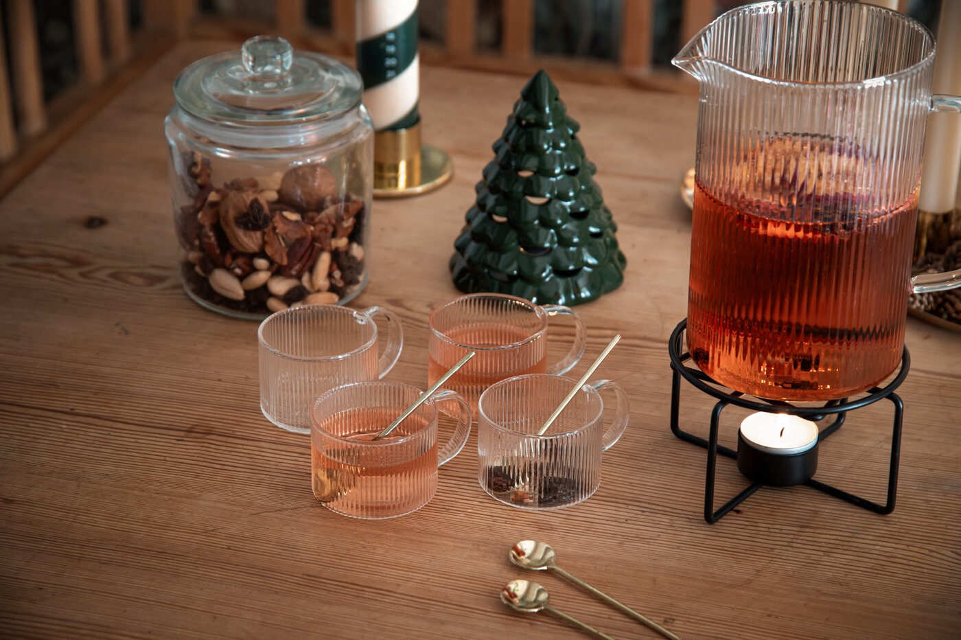 Räfflade glöggmuggar i glas på träbord med juldekorationer.