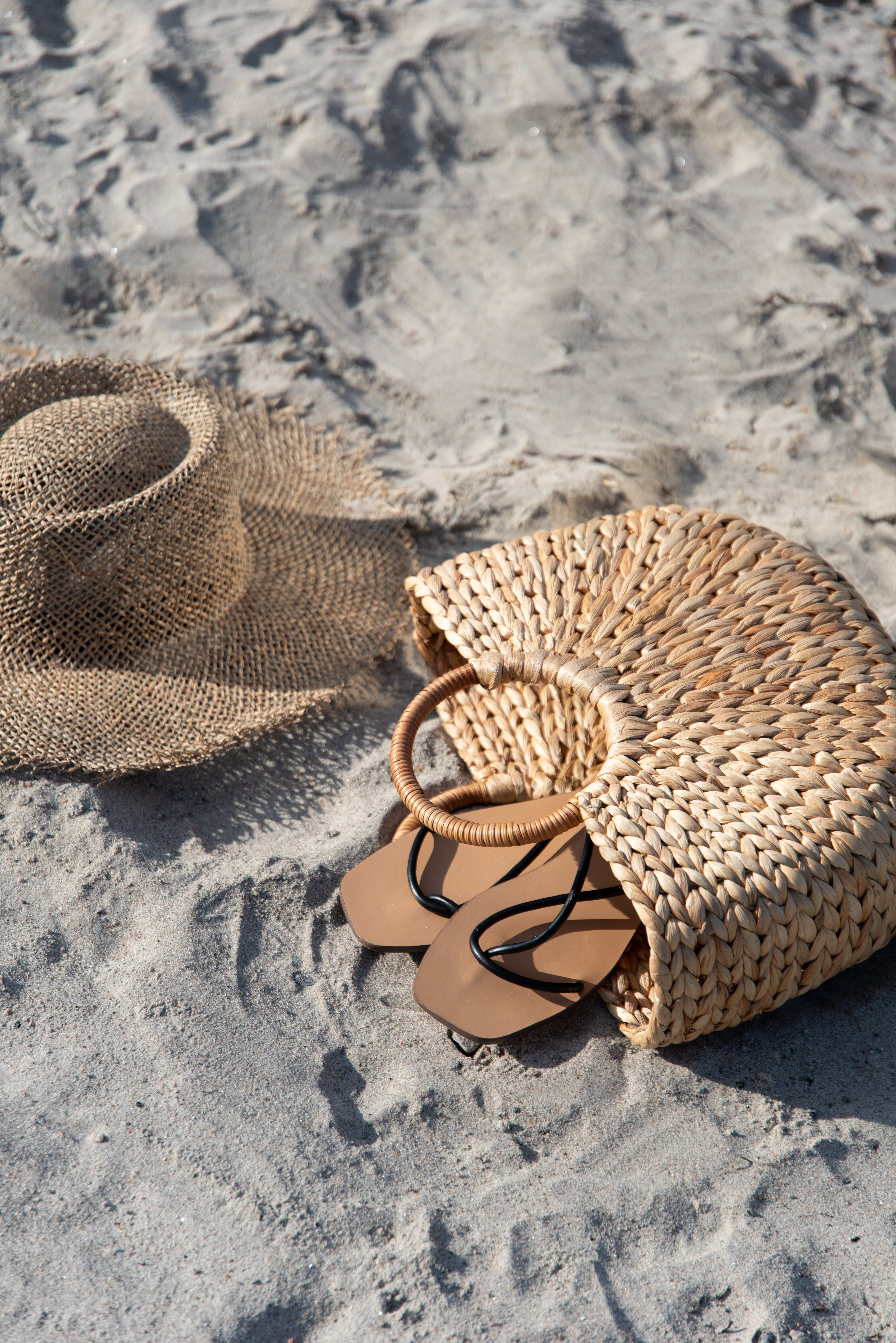 Stråväska, hatt och tofflor på stranden.