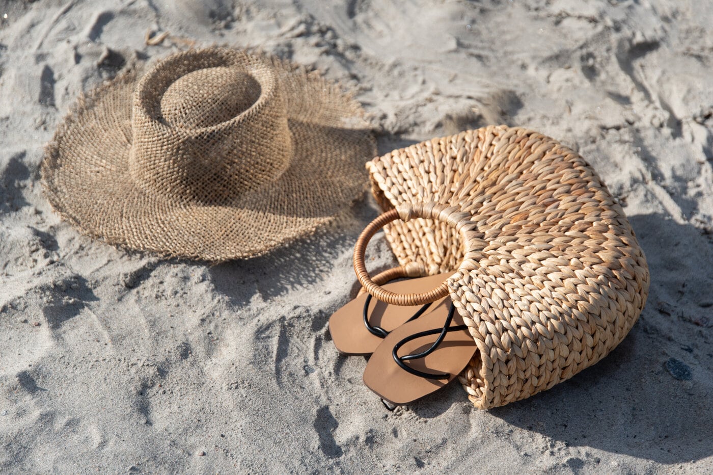 Solhatt, stråväska och sandaler i sanden.
