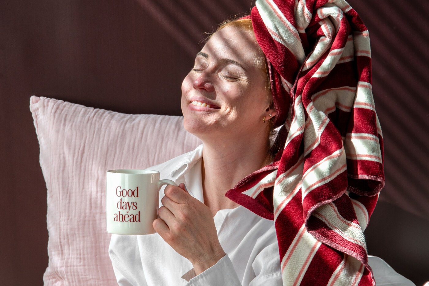 Kvinna kopplar av med en mugg och en röd- och vitrandig handduk virad runt huvudet.