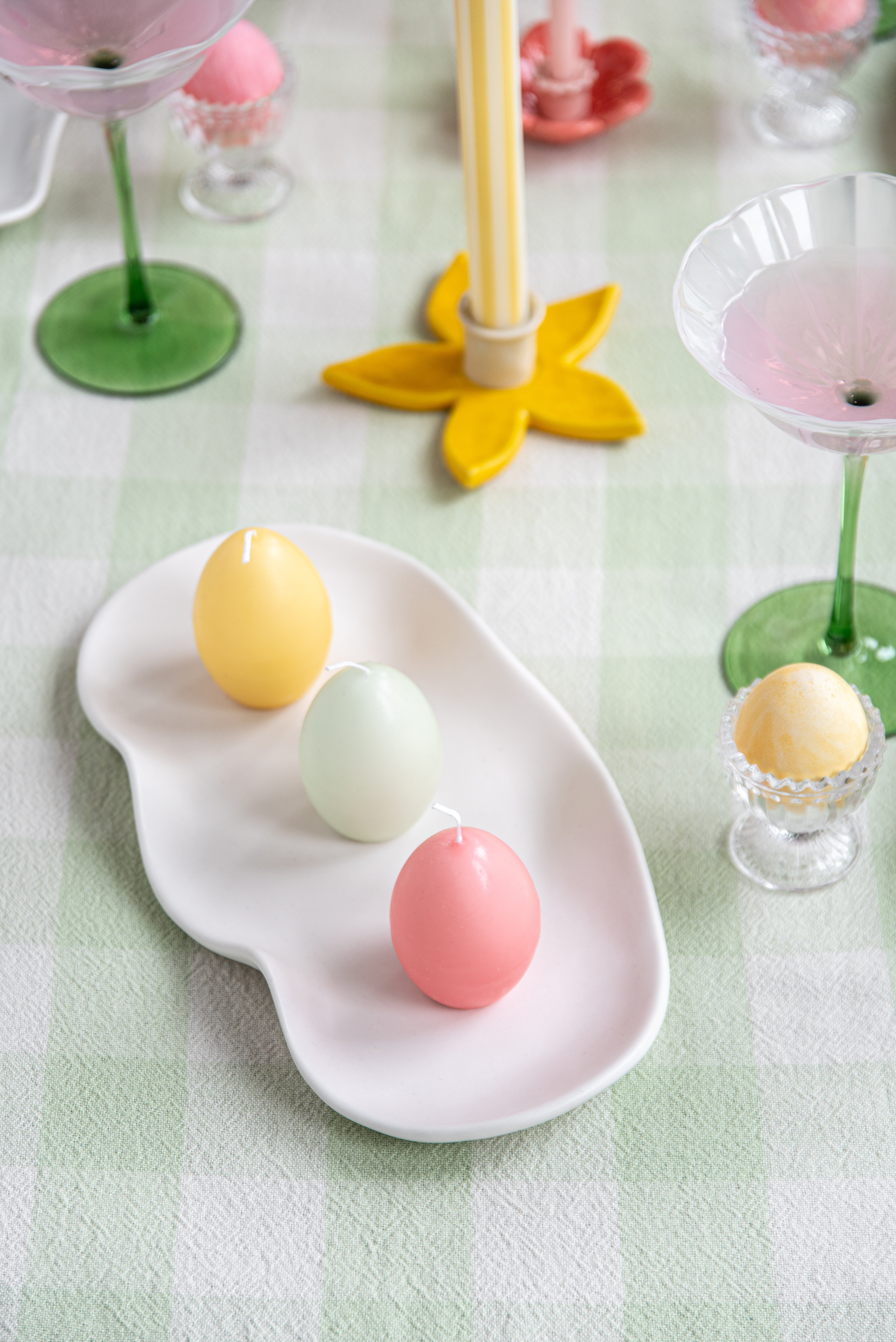 Äggformade ljus på vitt ljusfat på dukat påskbord.