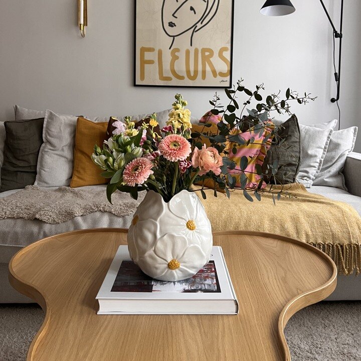 Vas med blommor i placerad på ett soffbord i vardagsrum.