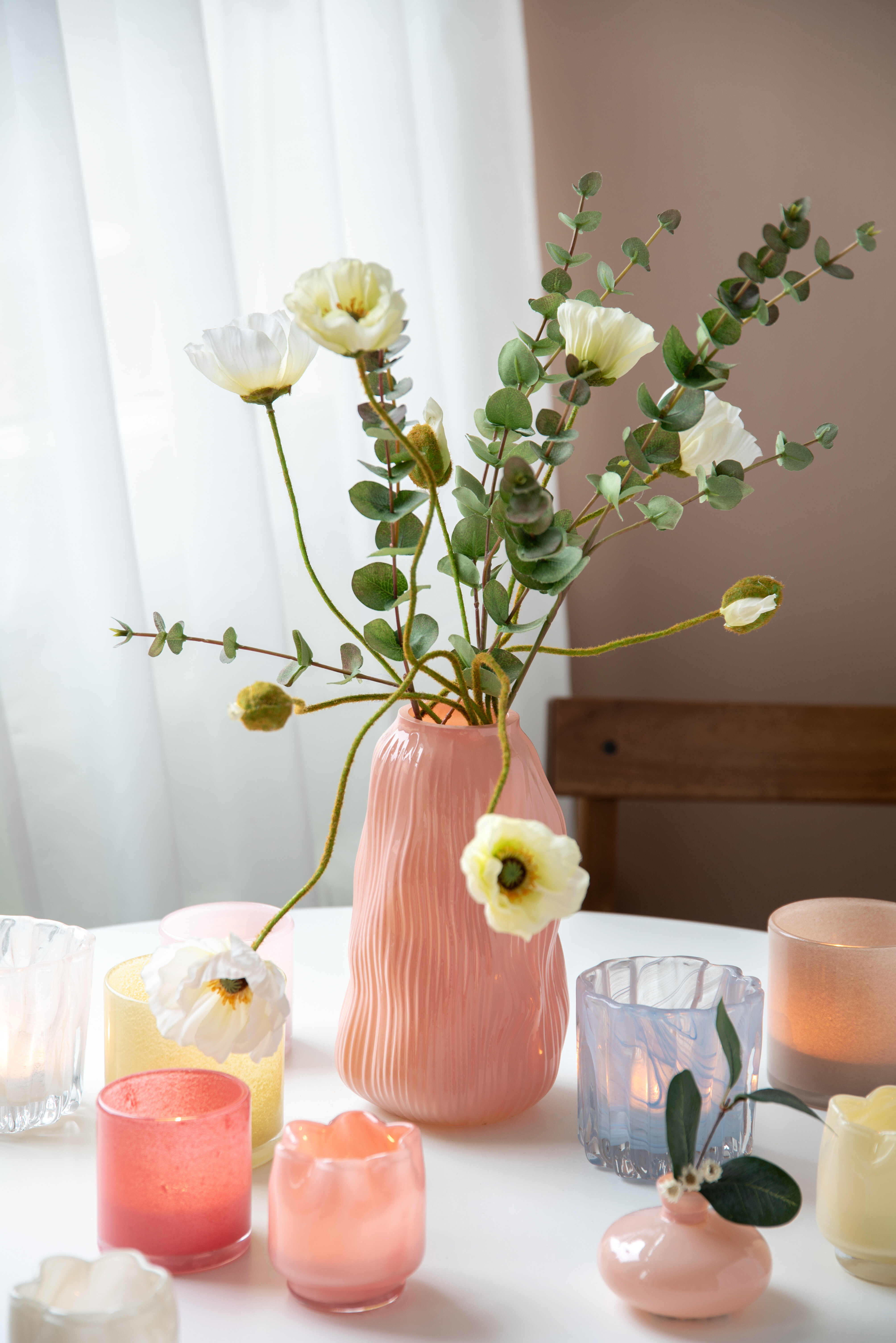 Rosa vas med konstväxter på bor dmed färgglada ljuslyktor