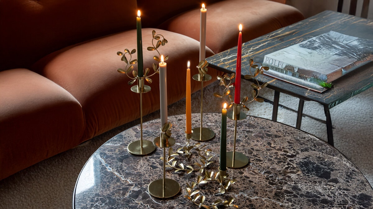 Guldiga ljusstakar med tända färgade kronljus på ett marmorbord.