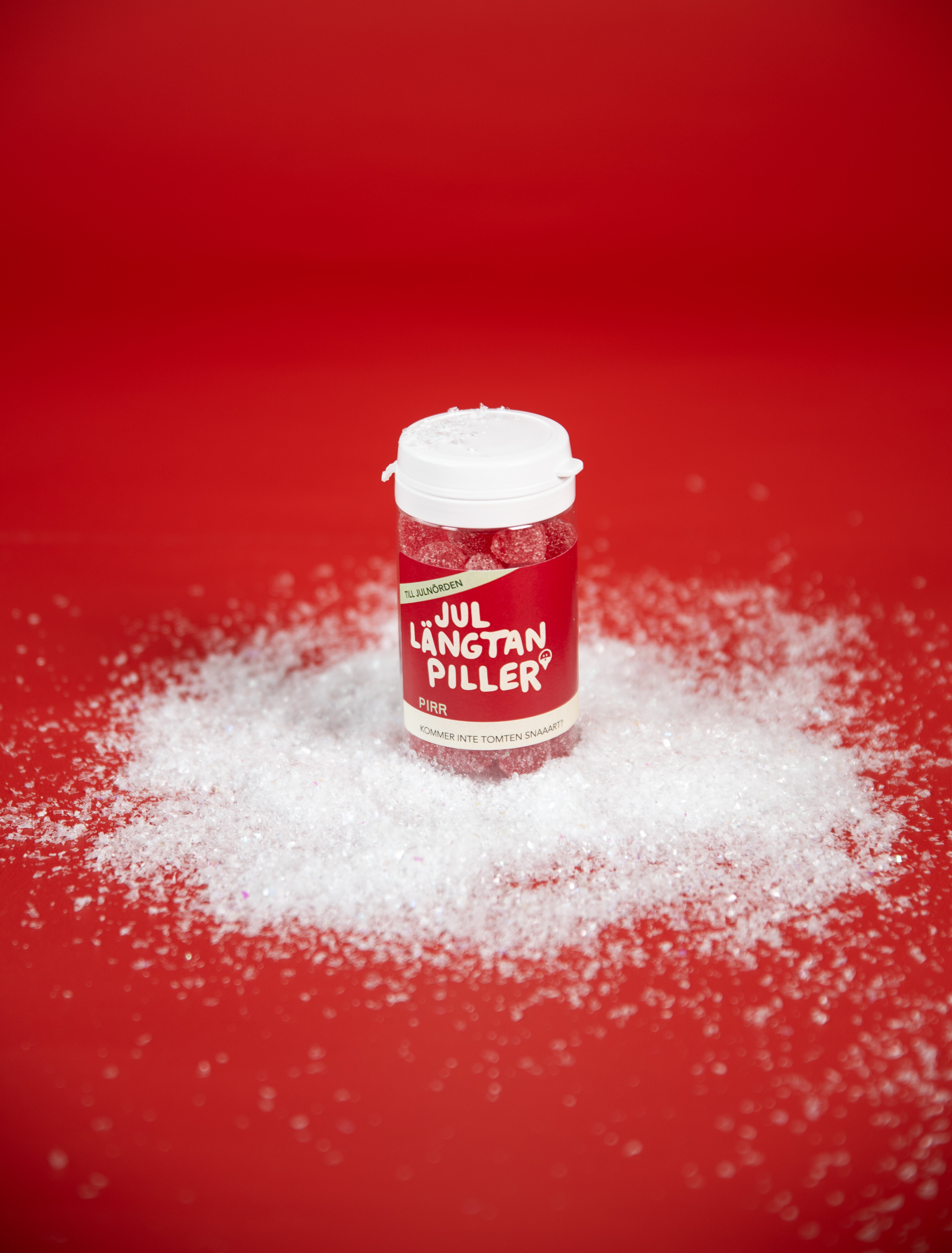 Burk med godis märkt Jullängtanpiller på röd bakgrund med konstsnö.