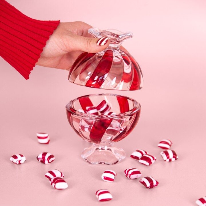 Rödvitt julgodis i glasskål mot rosa bakgrund.