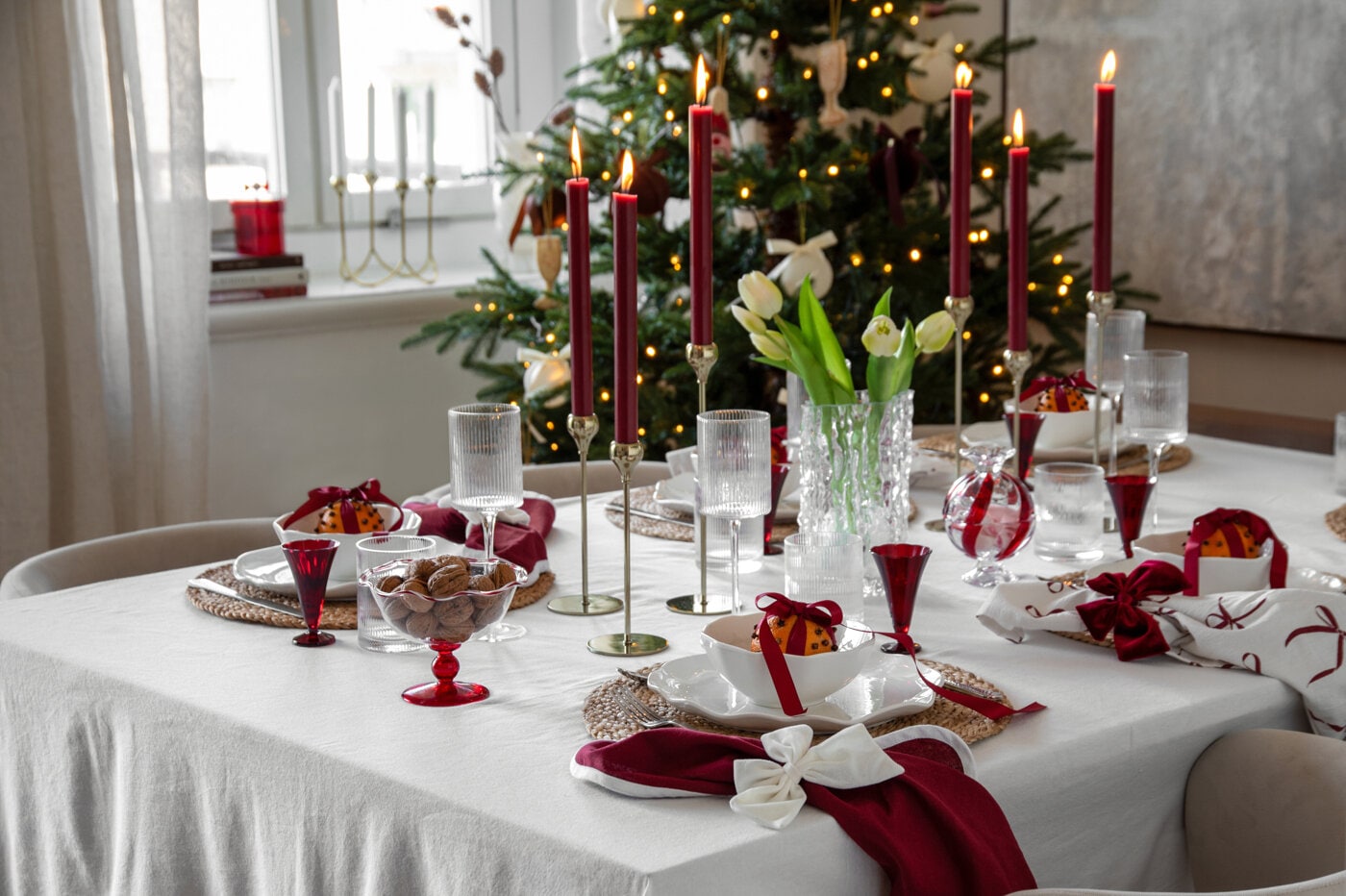 Juldukning i vinrött och vitt med levande ljus, glas och dekorativa rosetter.