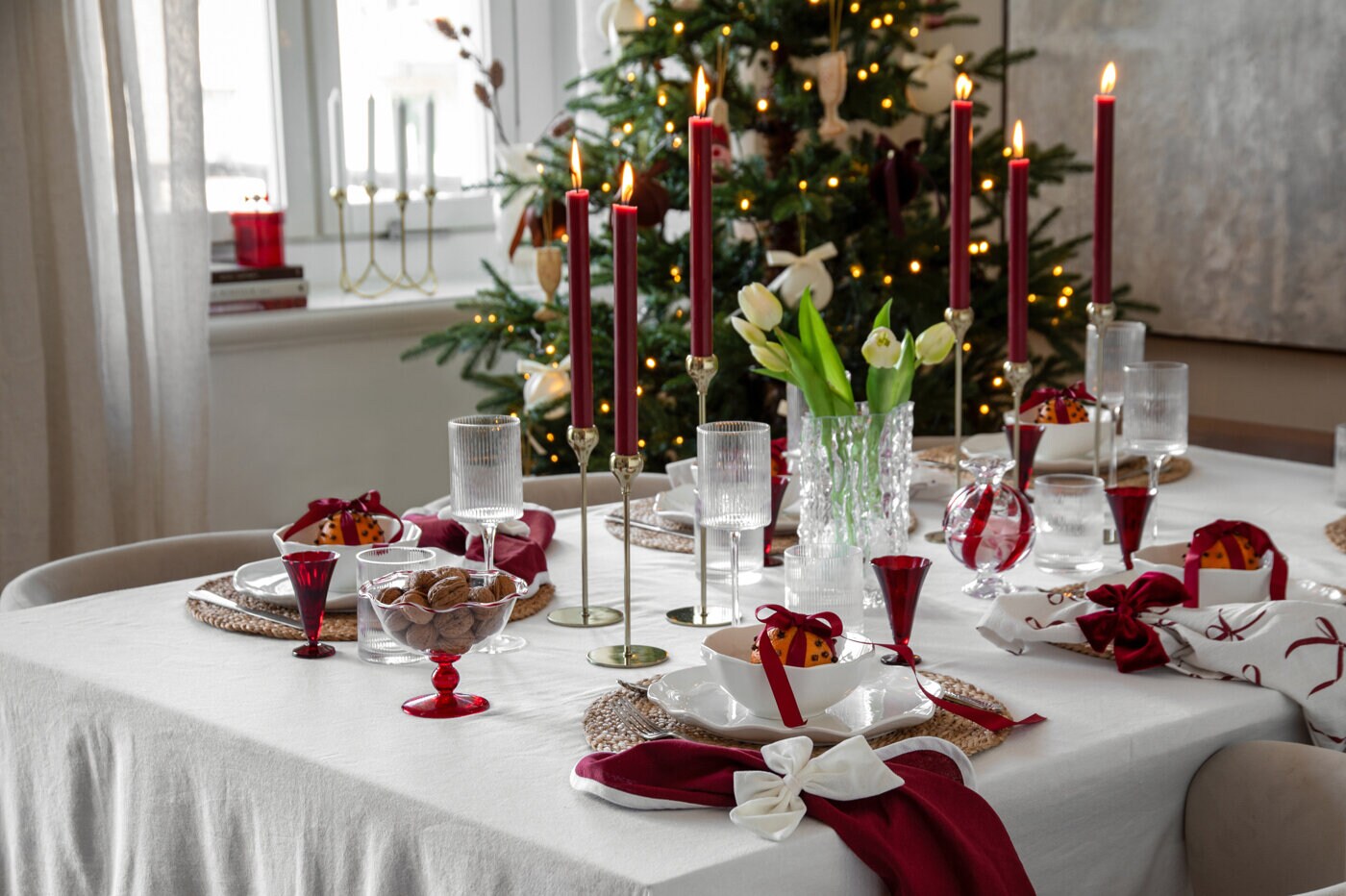 Traditionell juldukning i vinrött och vitt med levande ljus, glas och dekorativa rosetter.