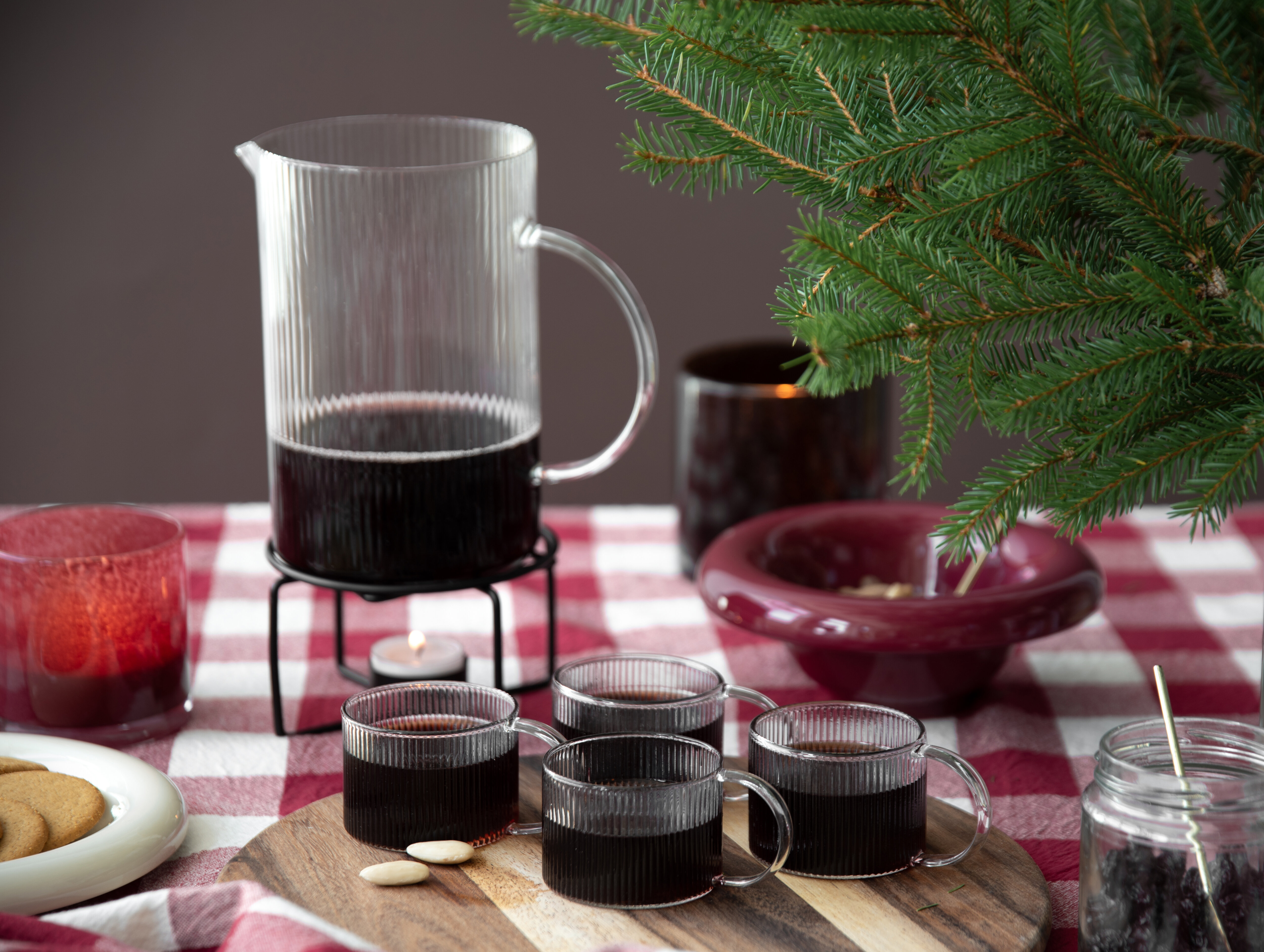 Glögg serverad i glaskanna och glasmuggar på juldukning med granris.