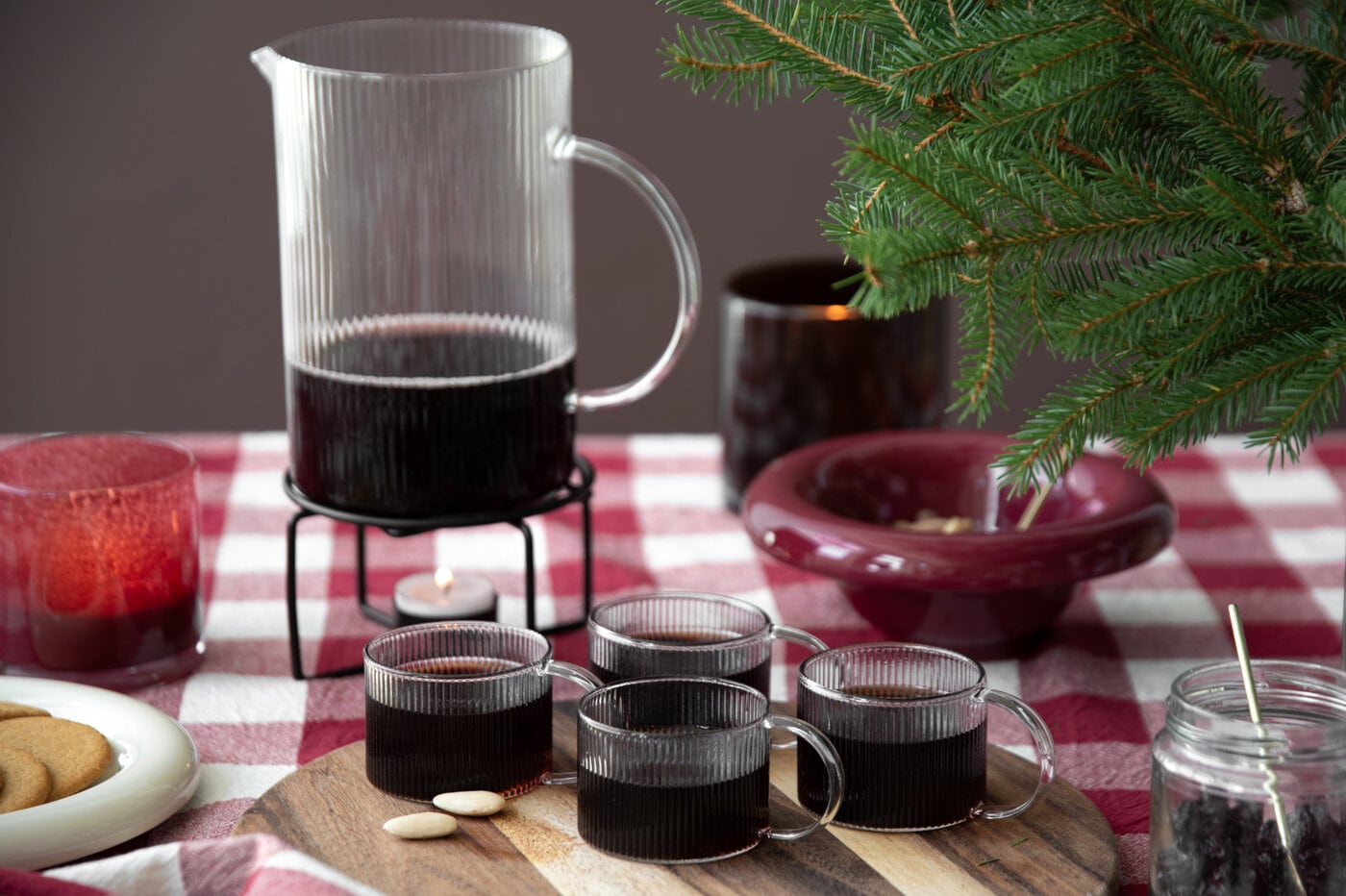 Glögg i glaskanna och glas på juldukning.