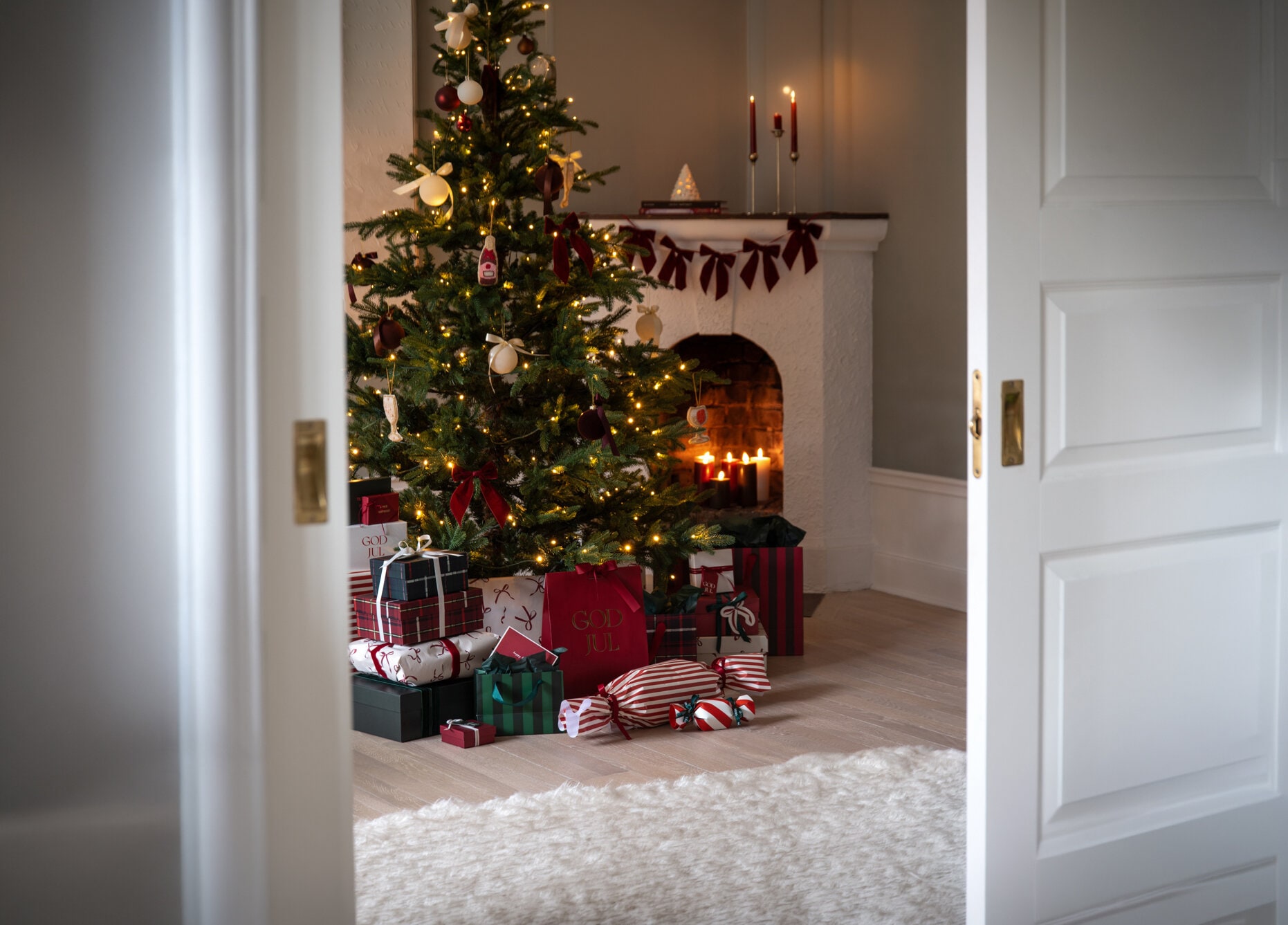 Klädd julgran med julbelysning och inslagna julklappar framför en öppen spis.