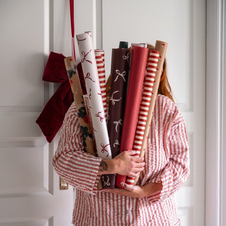 Person som håller flera rullar julklappspapper i röda och vita mönster.