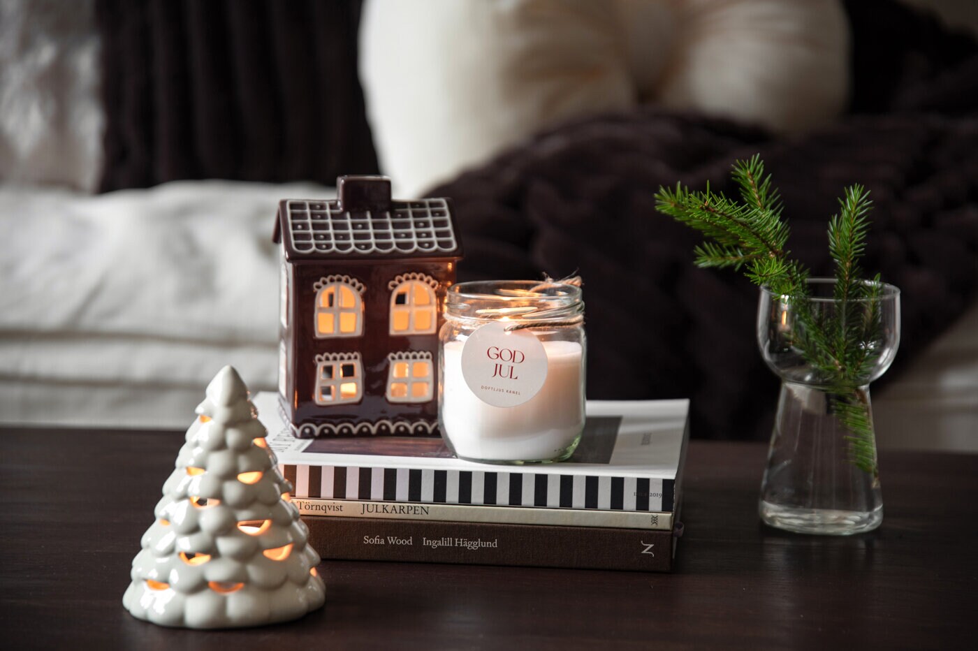 Juldekorationer med lysande pepparkakshus, julgran och doftljus på ett bord.
