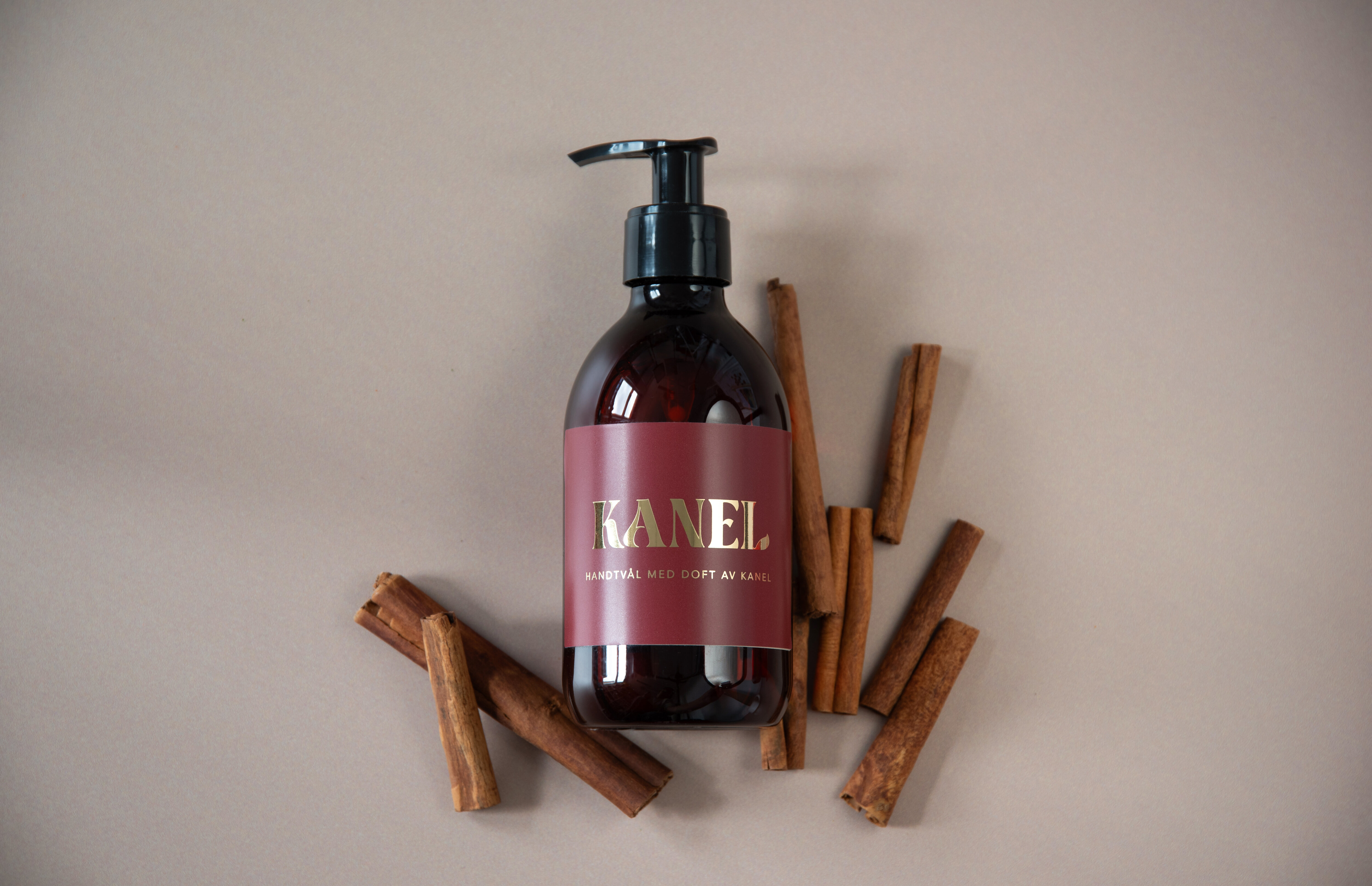 Pumpflaska med kaneltvål omgiven av kanelstänger.