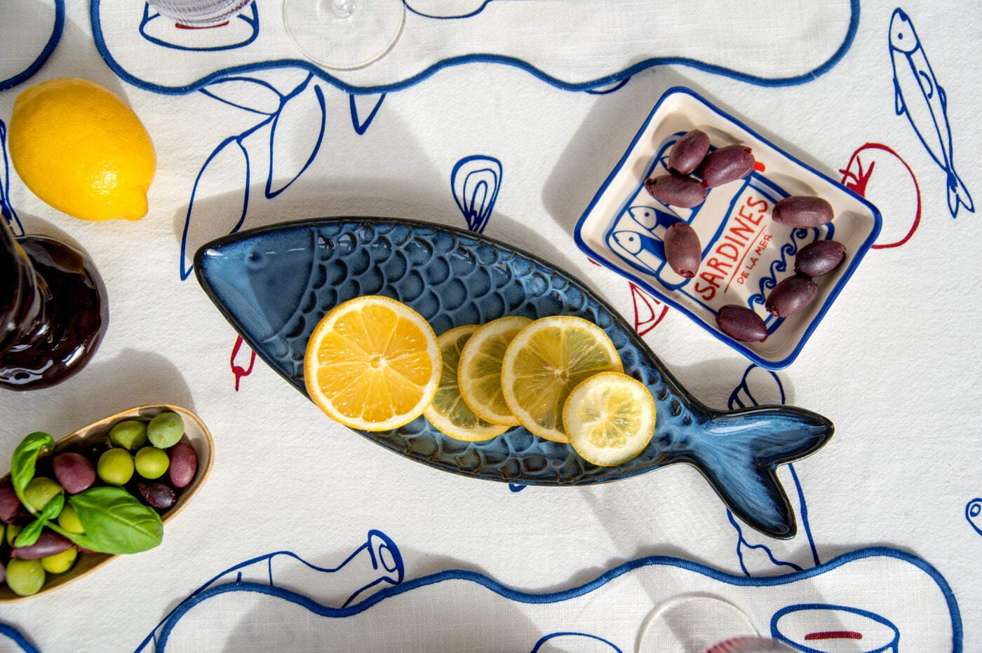Fiskformat serveringsfat med citronskivor på mönstrad duk med oliver och småplock.
