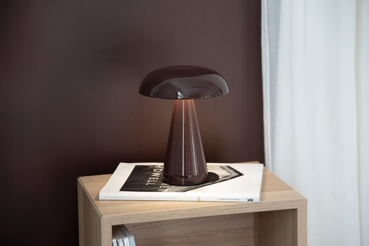 Brun bordslampa på ett sidobord mot en mörkbrun vägg.