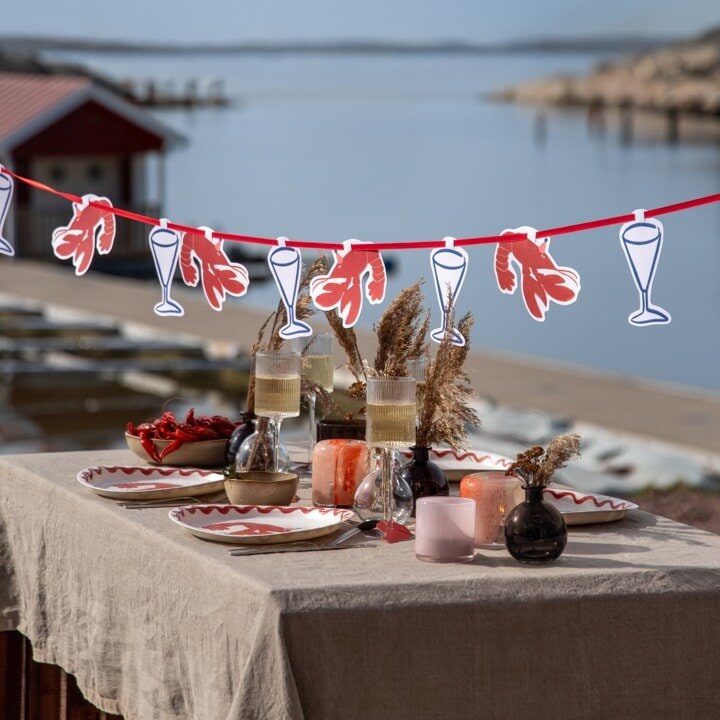 Kräftskivedukning utomhus med kräftgirlang, dukat bord och sjöutsikt.