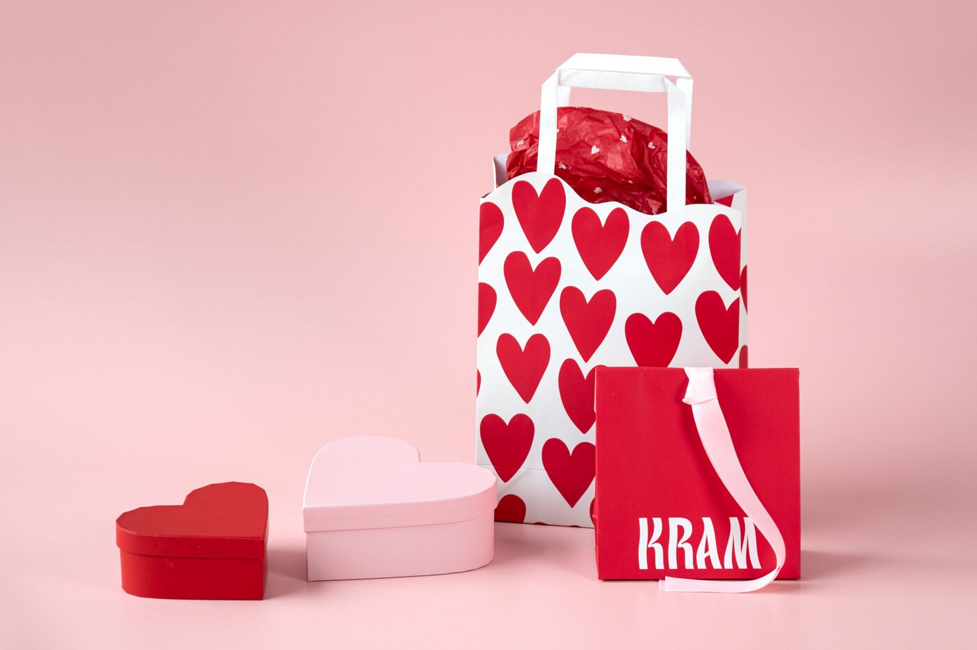 Presentpåsar och hjärtformade askar i rött och rosa mot rosa bakgrund.