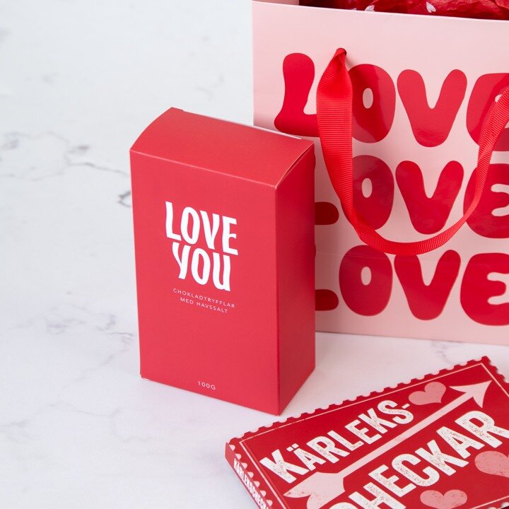 Chokladtryffel i röd presentförpackning och presentpåse bakom.