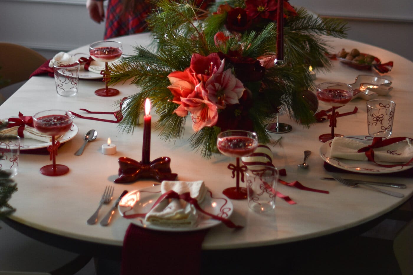 Juldukning med röda ljus, glas och servetter, centrerad kring en blomsterdekoration med amaryllis och grankvistar.