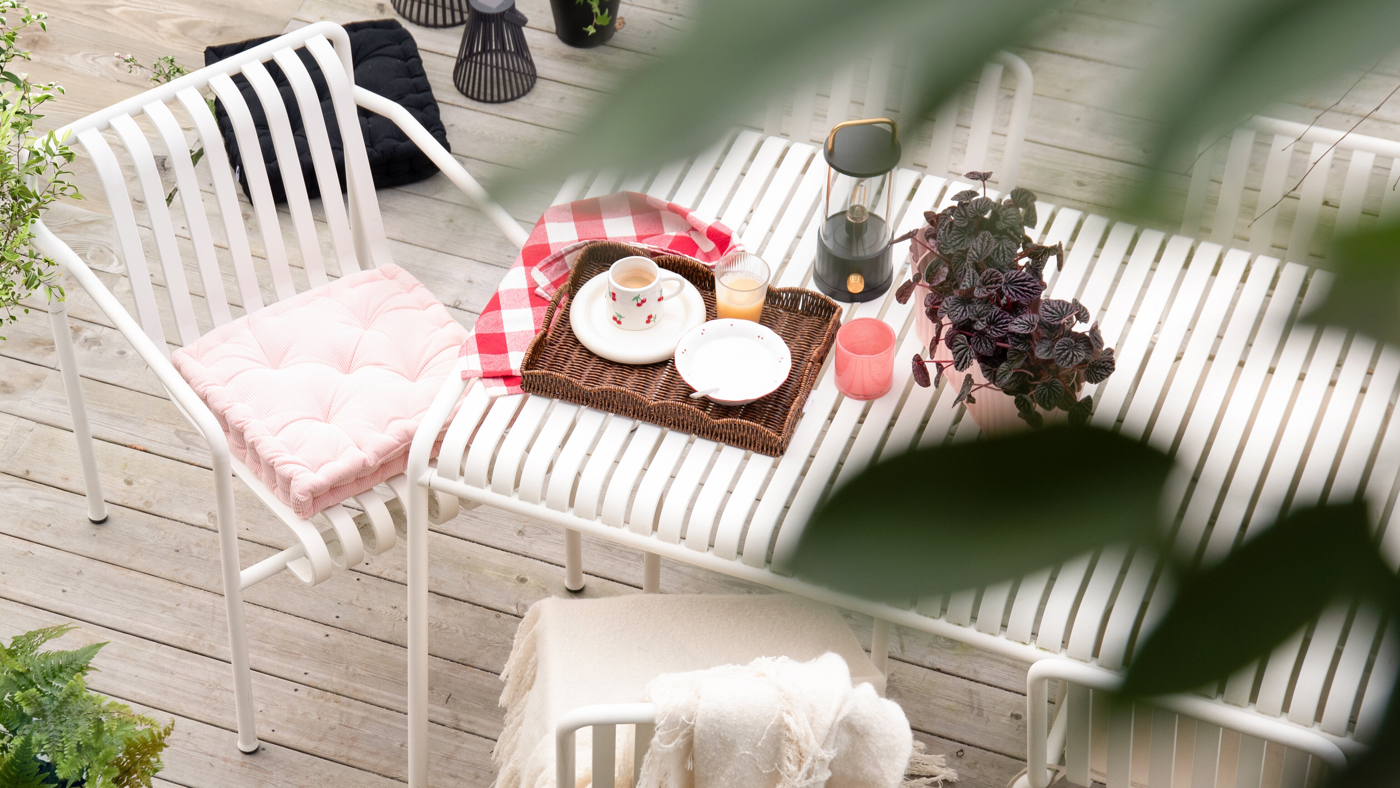 Dukat bord på balkong eller uteplats med bricka, kopp, ljus och växter.
