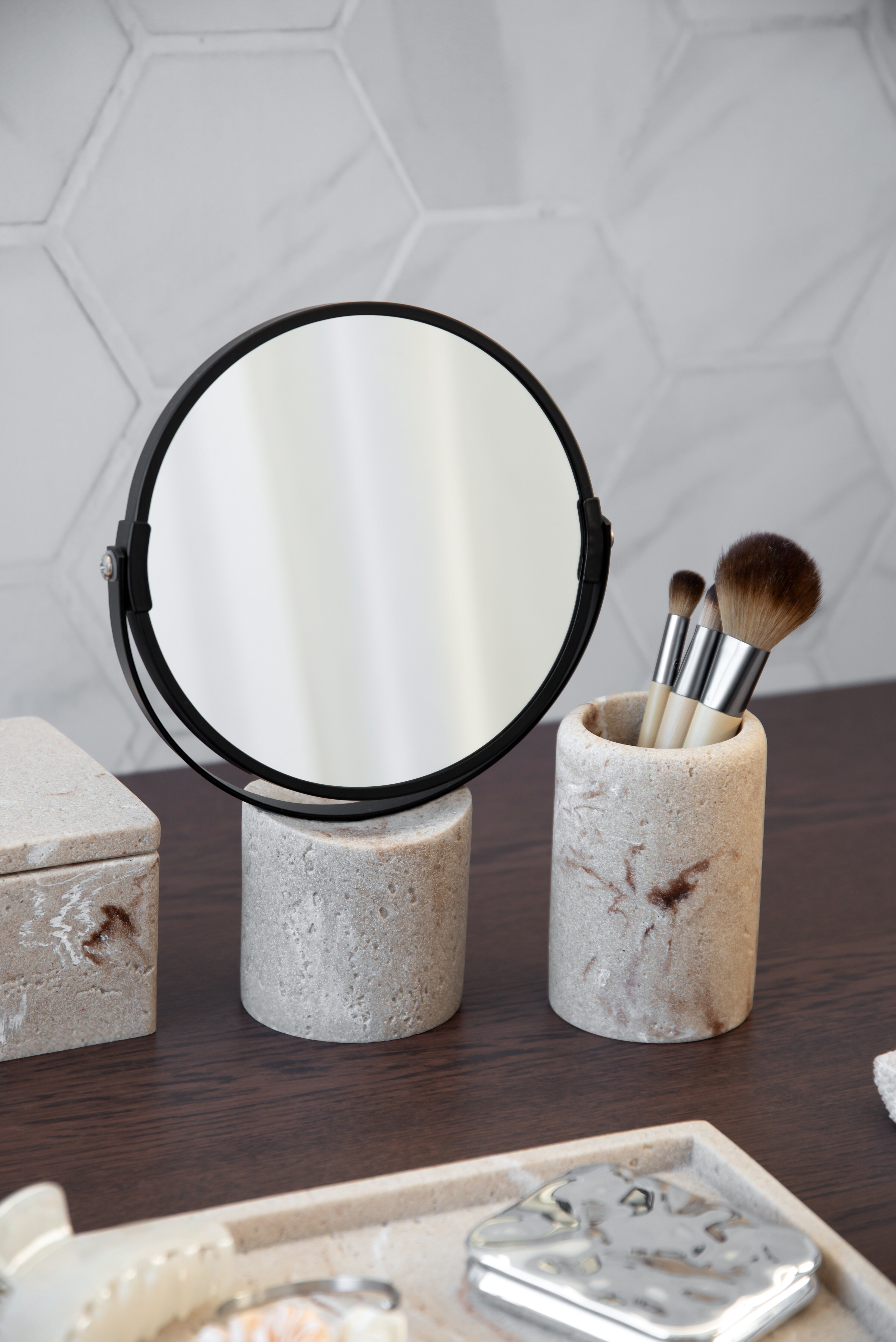 Rund spegel på fot tillsammans med marmorerade behållare och sminkborstar.