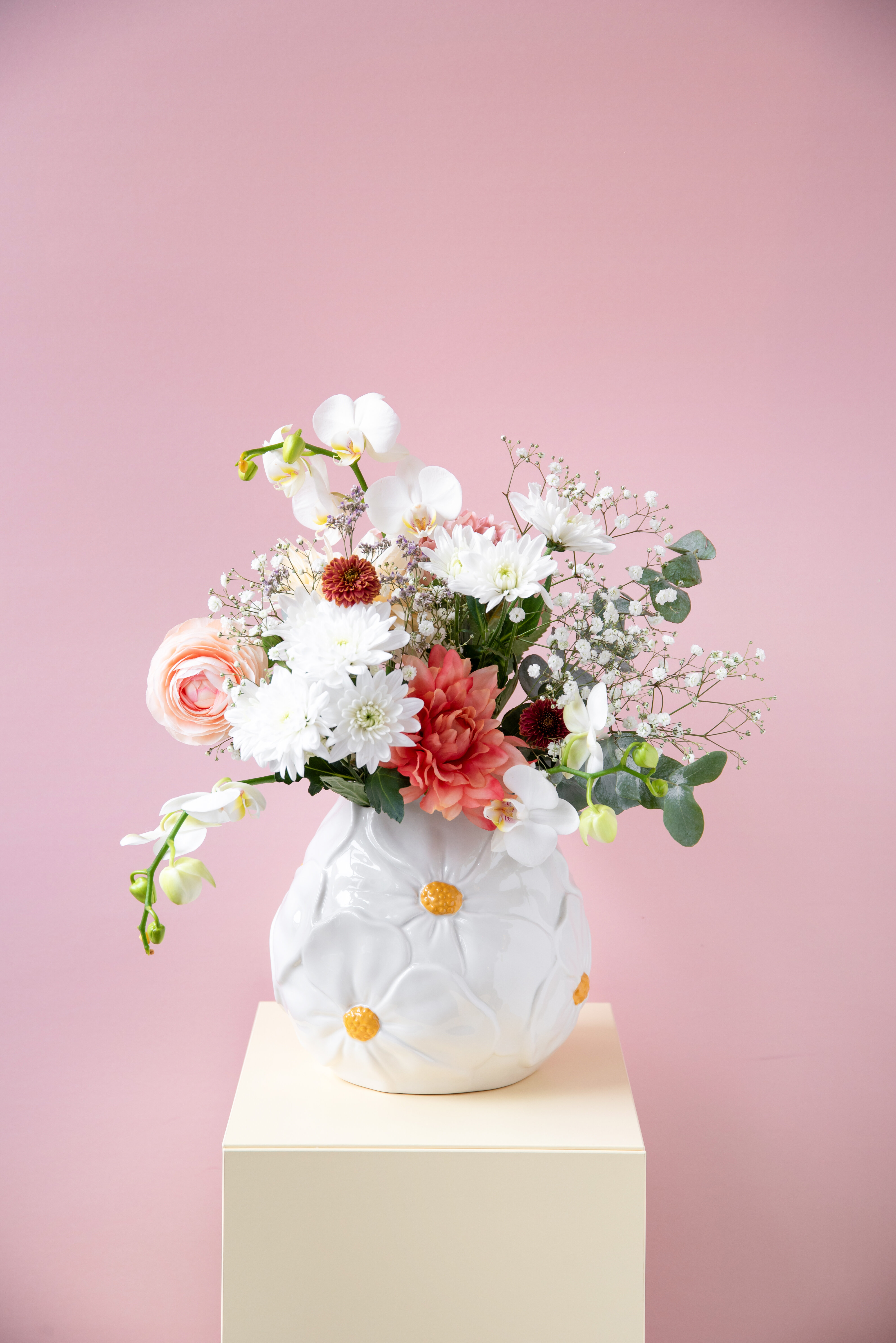 Vas med blommor i på piedestal mot rosa bakgrund.