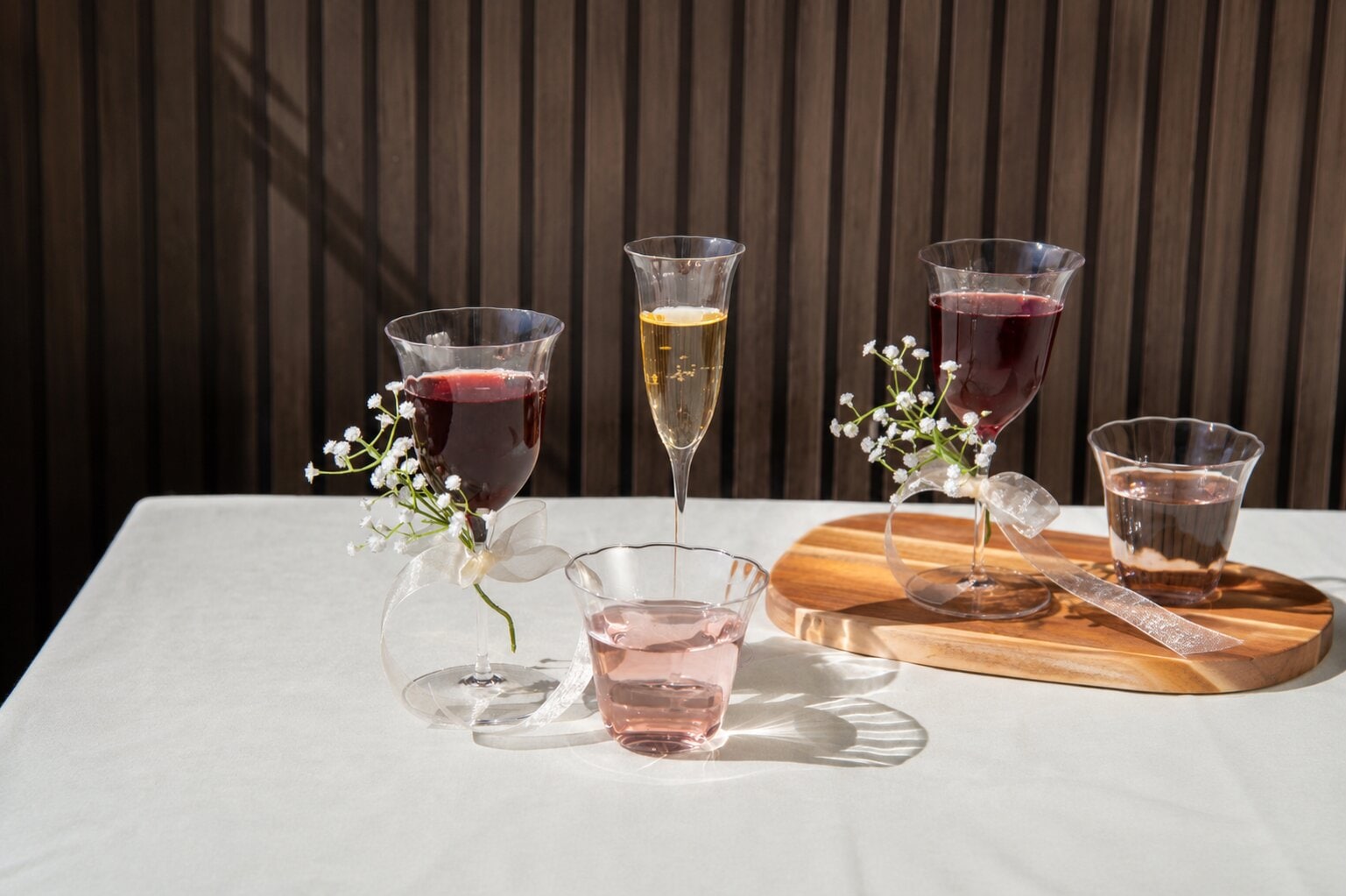 Dukat bord med vinglas, champagneglas och dricksglas samt små vita blommor i solljus.
