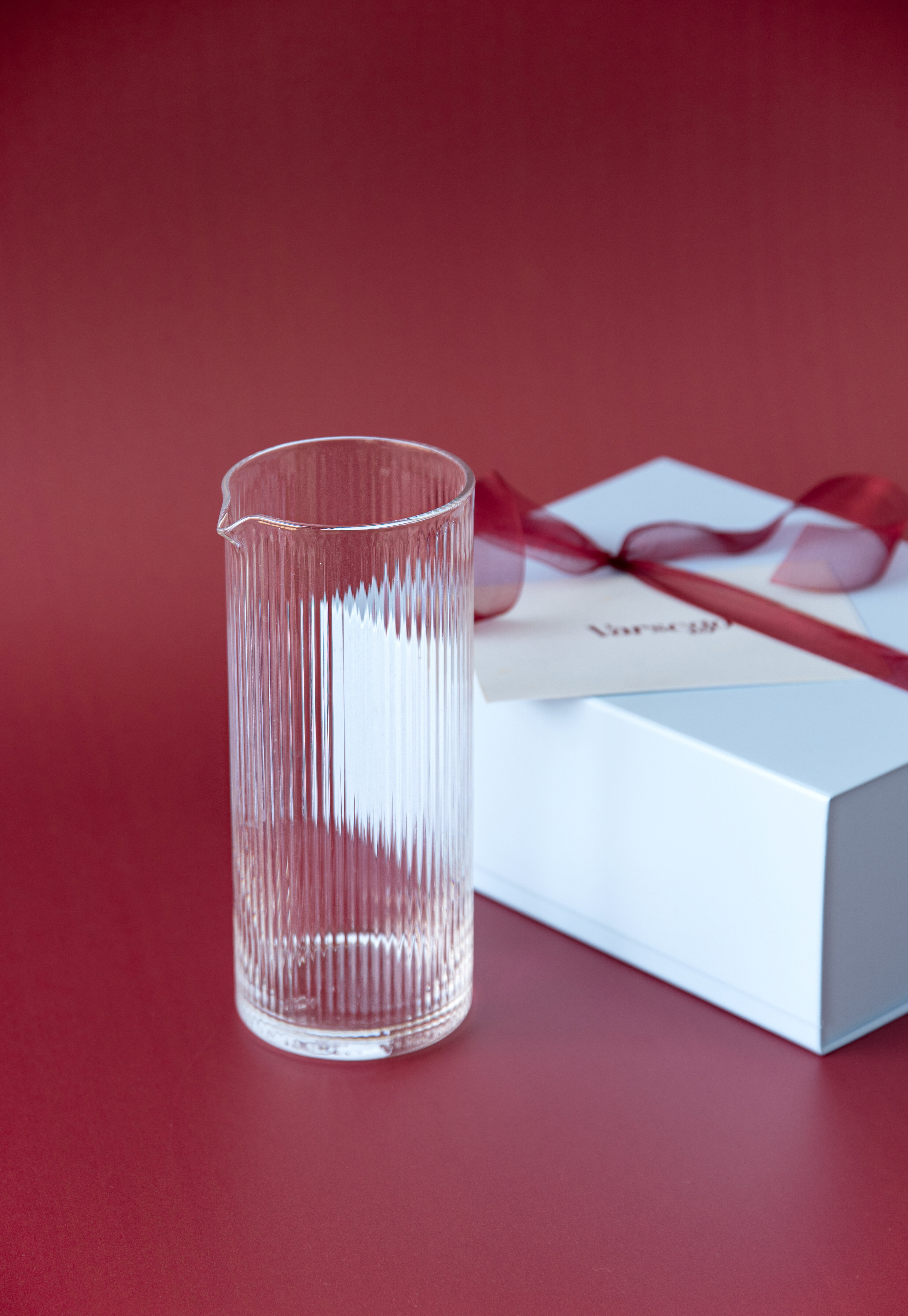 Ribbad glaskanna framför en blå presentförpackning.