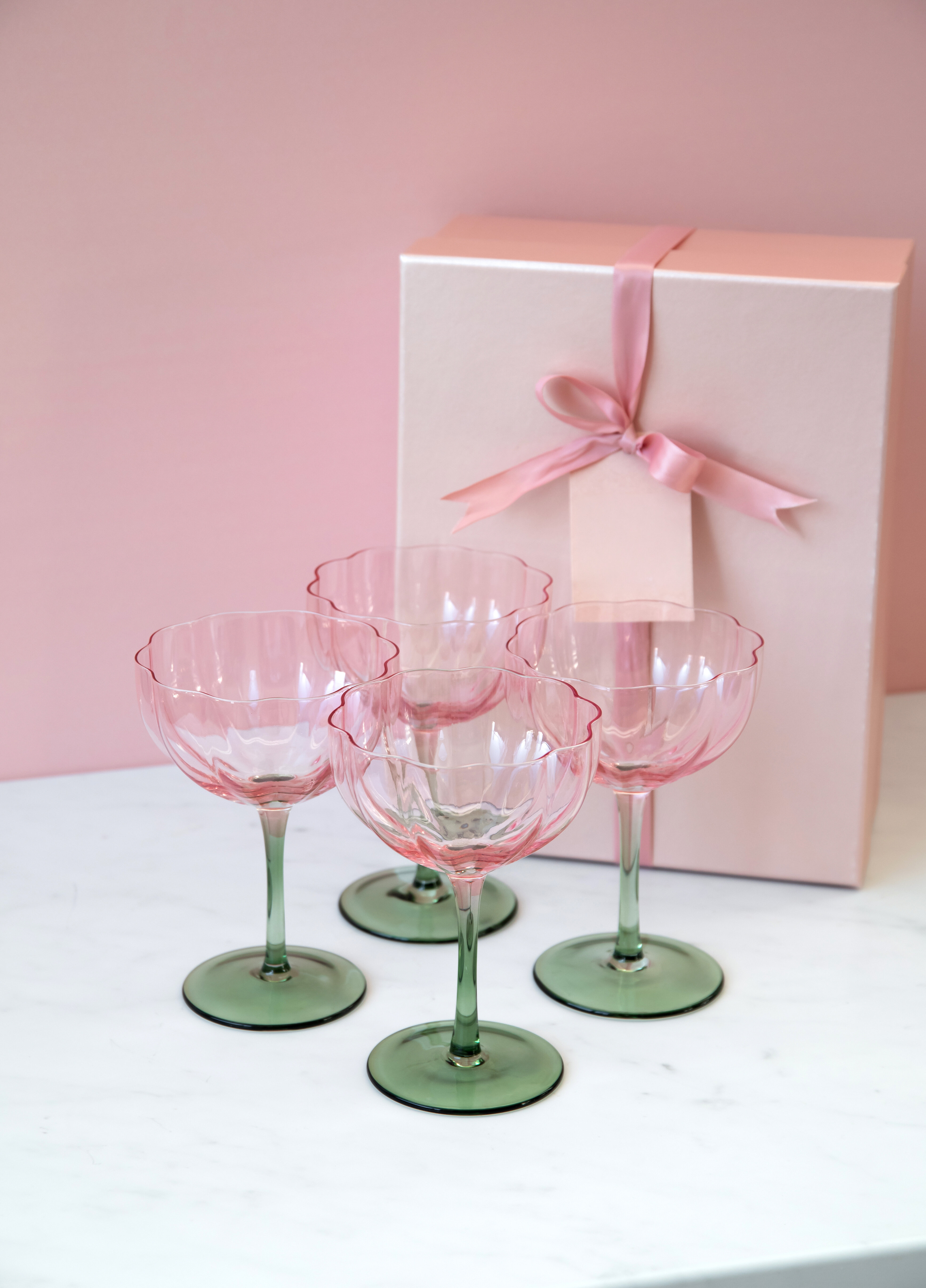 Rosa/gröna coupeglas framför rosa presentbox.