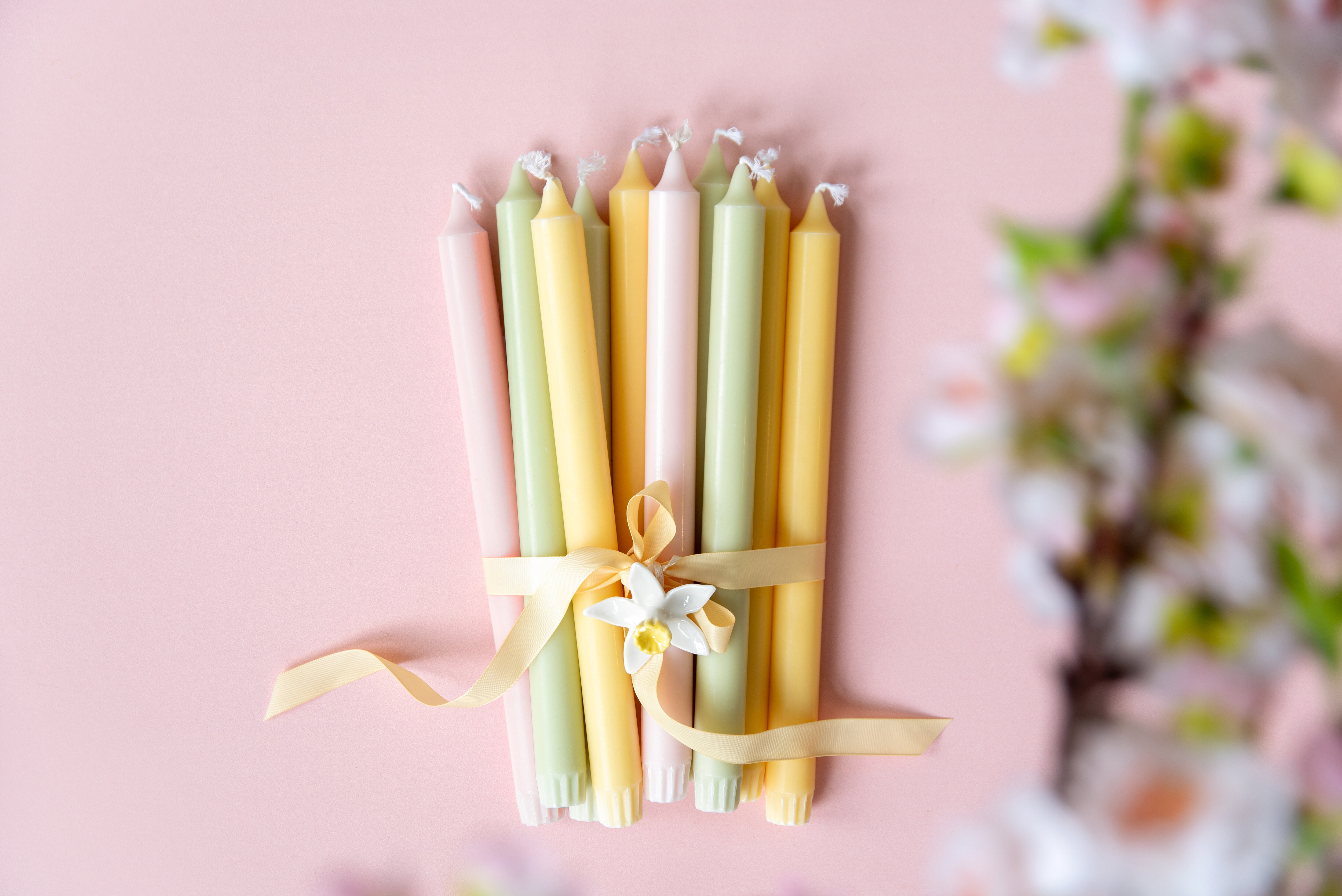Tända pastellfärgade ljus i blommformade ljusstakar på ett bord.
