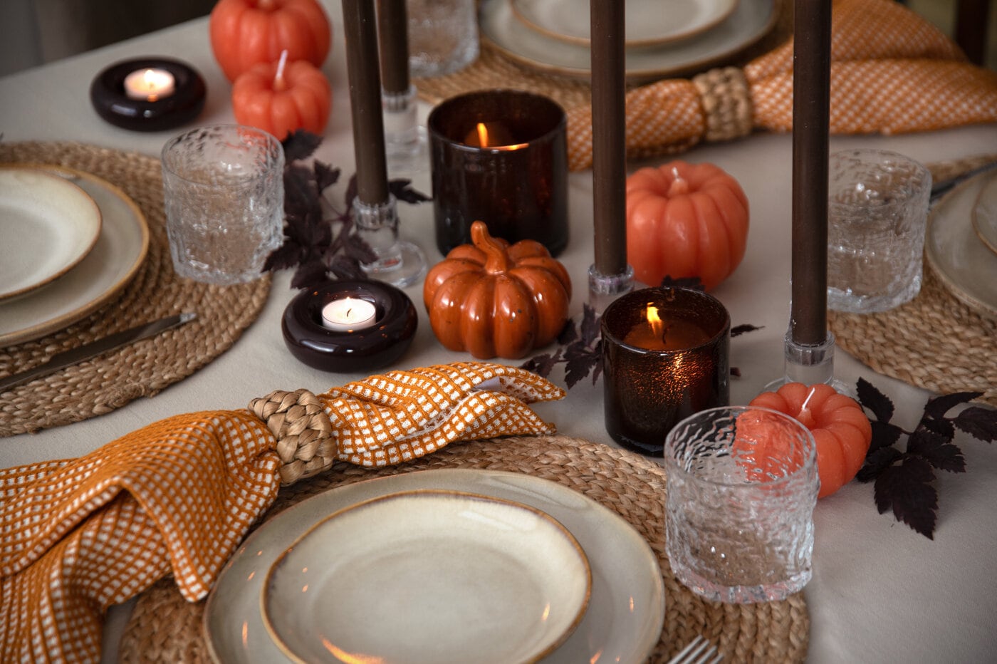 Dukat bord med porslin, glas, servetter, ljus och dekorativa pumpor i varma toner.