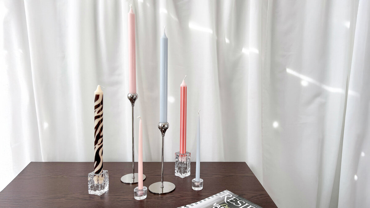 Flera ljusstakar i metall och glas med höga stearinljus i olika färger.