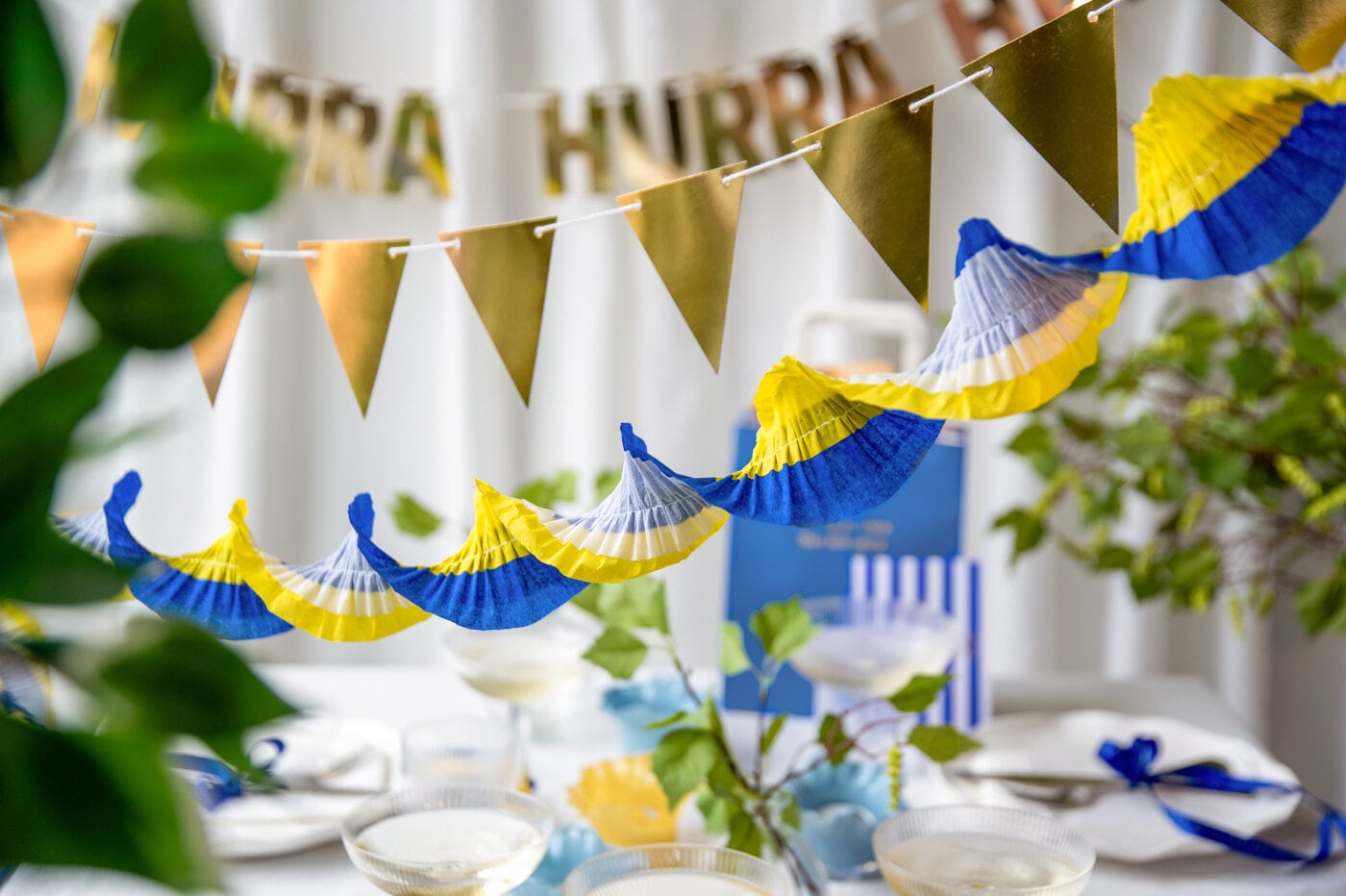 Blå‑gula studentdekorationer med vimplar och pappersgirlander över ett dukat bord inför studentfirande.