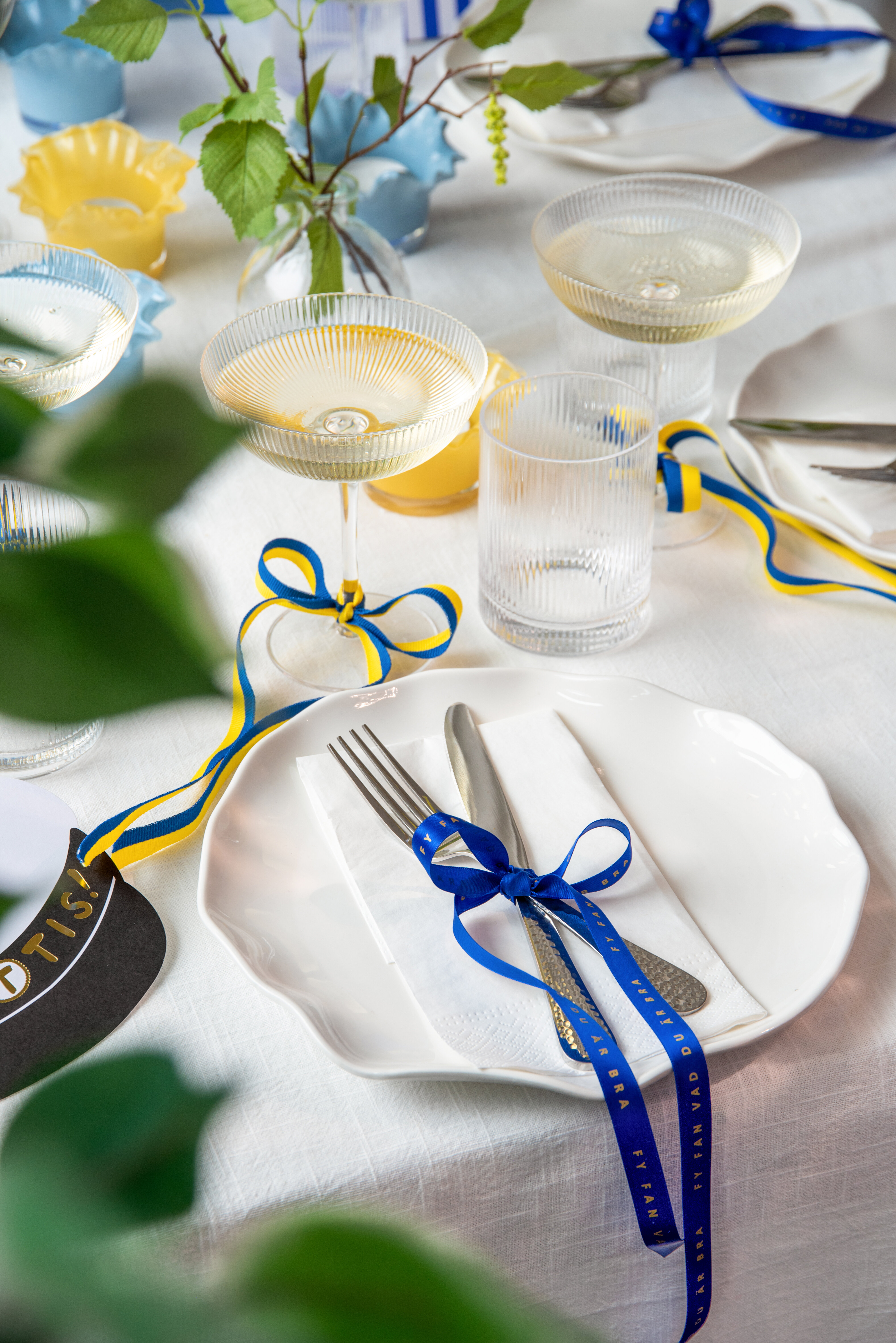 Dukat bord med glas, servetter och blå‑gula band.