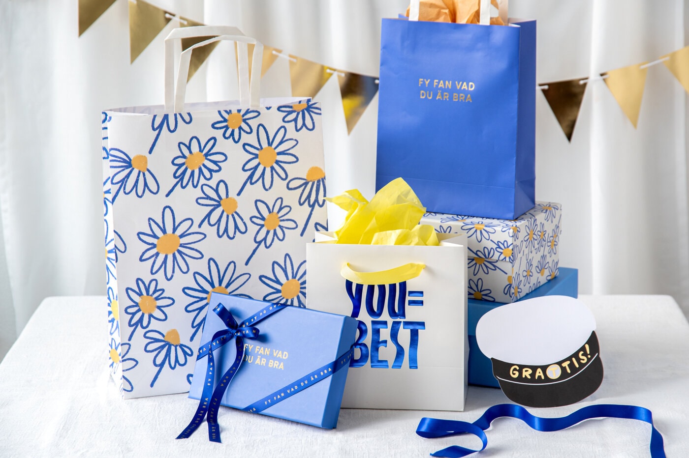 Presentpåsar och paket i blått och vitt med prästkragemönster, gul silkespapper och studentinspirerade detaljer.