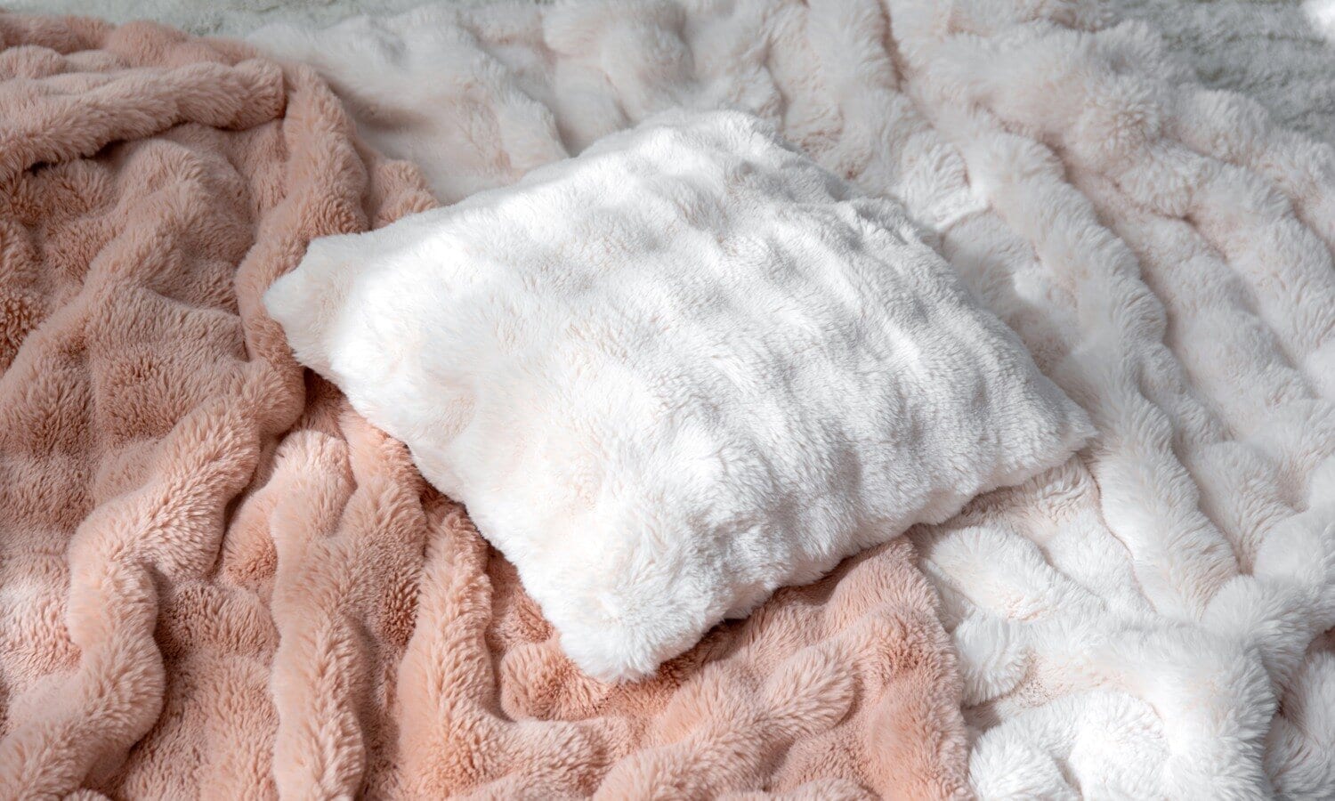 Mjuka plädar och en fluffig kudde i ljusa toner, stylade som inspiration för ett ombonat hem.
