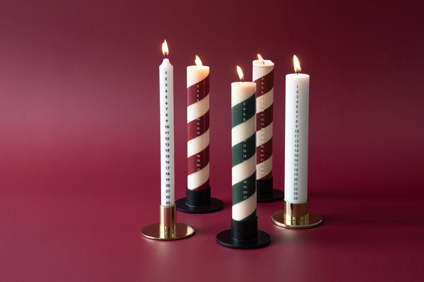 Adventsljus med datum i rött, grönt och vitt på mörkröd bakgrund.